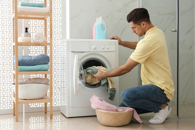 Photo of Man putting clothes into washing machine in bathroom. Laundry day