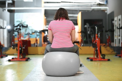 Overweight woman training with fitball in gym