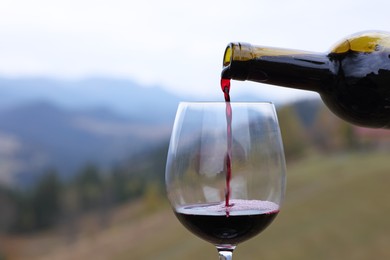 Photo of Pouring red wine into glass in mountains, closeup