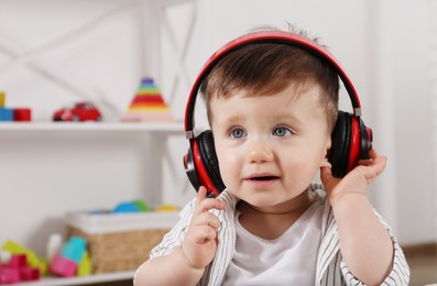 Photo of Cute little boy in headphones listening to music at home, space for text