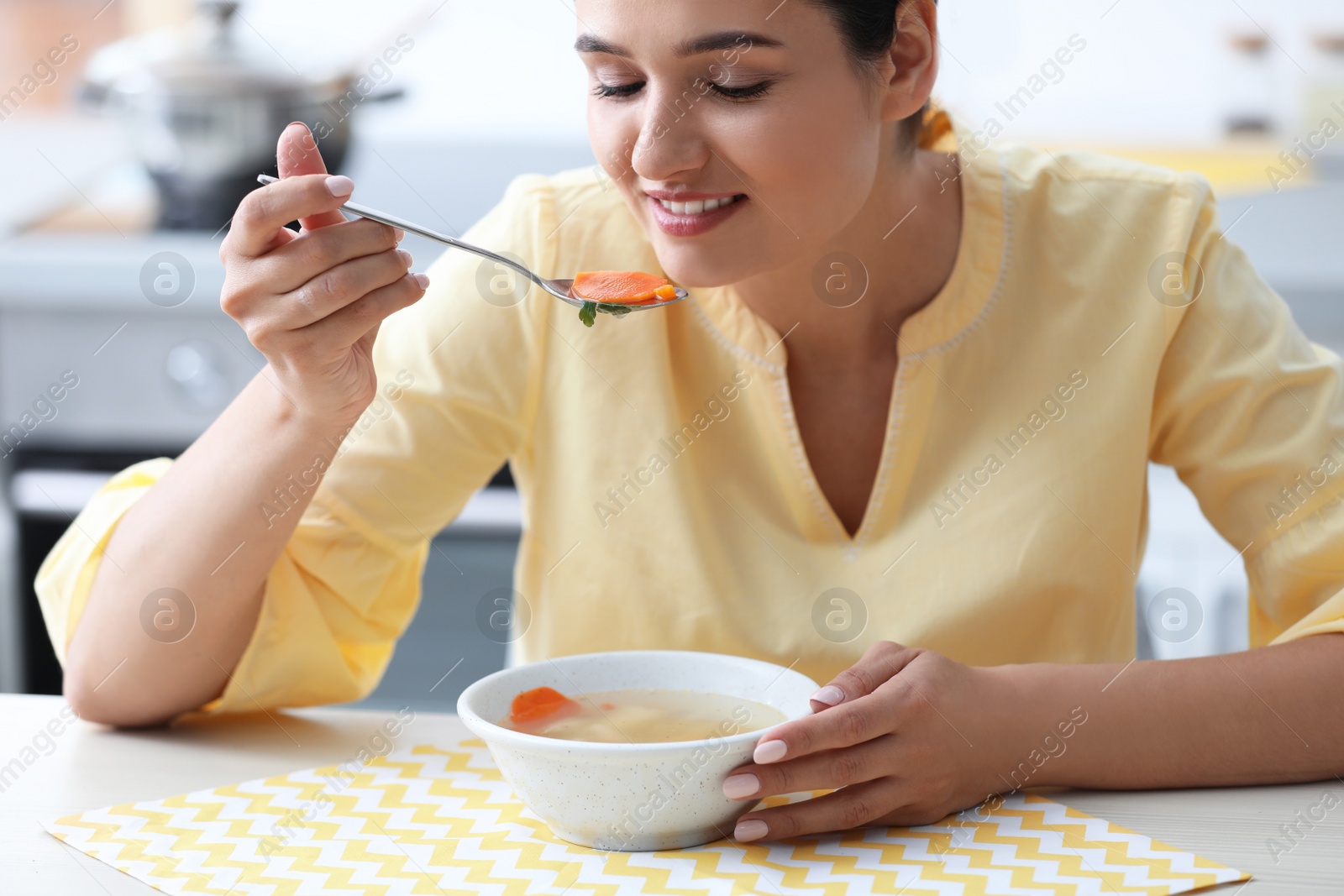 Photo of Young woman eating tasty vegetable soup at table in kitchen