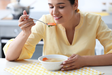 Young woman eating tasty vegetable soup at table in kitchen