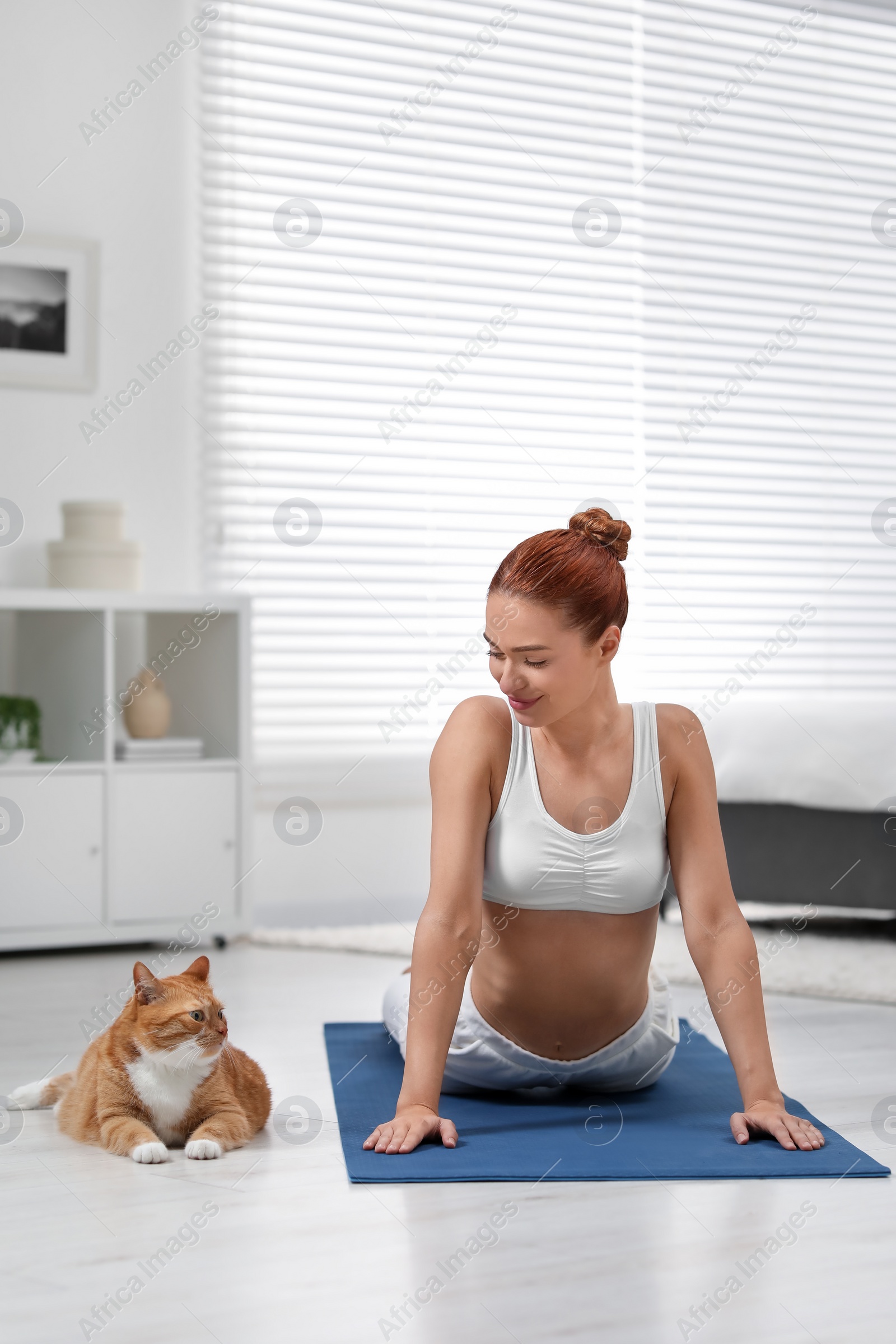 Photo of Beautiful woman with cute red cat practicing yoga on mat at home