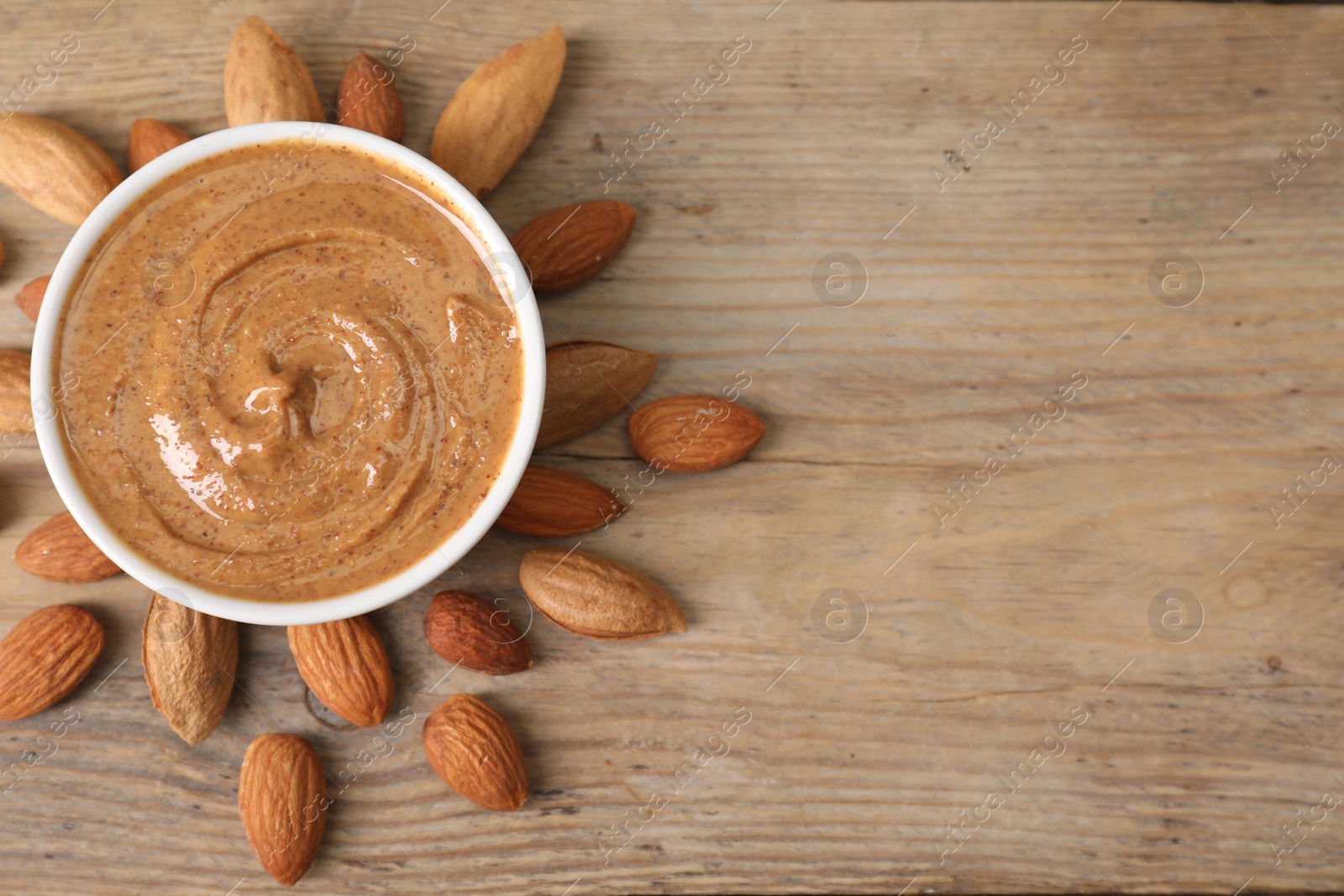 Photo of Delicious nut butter in bowl and almonds on wooden table, top view. Space for text