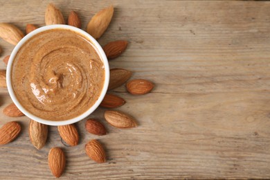 Delicious nut butter in bowl and almonds on wooden table, top view. Space for text