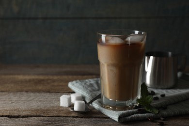 Glass of delicious iced coffee with milk, beans and sugar cubes on wooden table, space for text