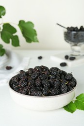 Bowl of delicious ripe black mulberries on white table