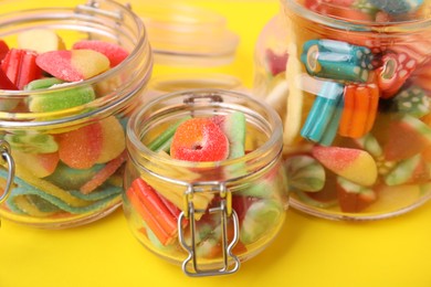 Photo of Glass jars of tasty colorful jelly candies on yellow background, closeup