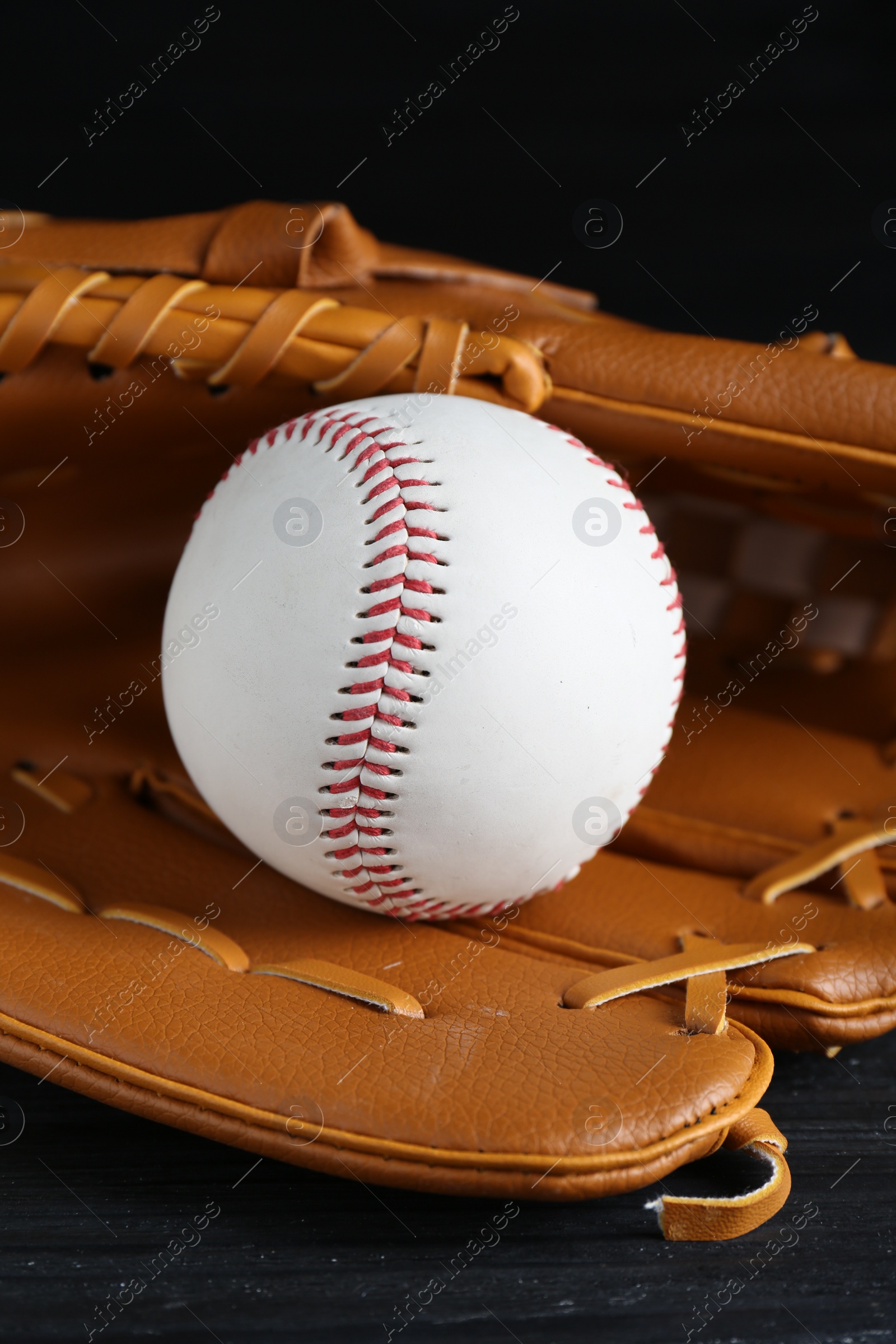 Photo of Catcher's mitt and baseball ball on black background, closeup. Sports game