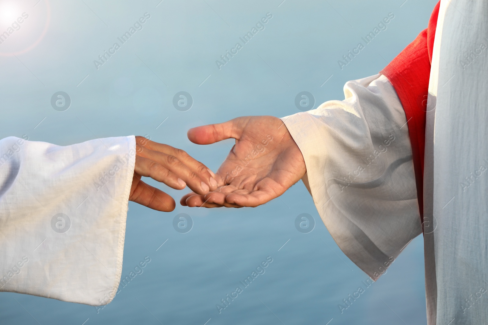 Photo of Man reaching for Jesus Christ's hand near water outdoors, closeup