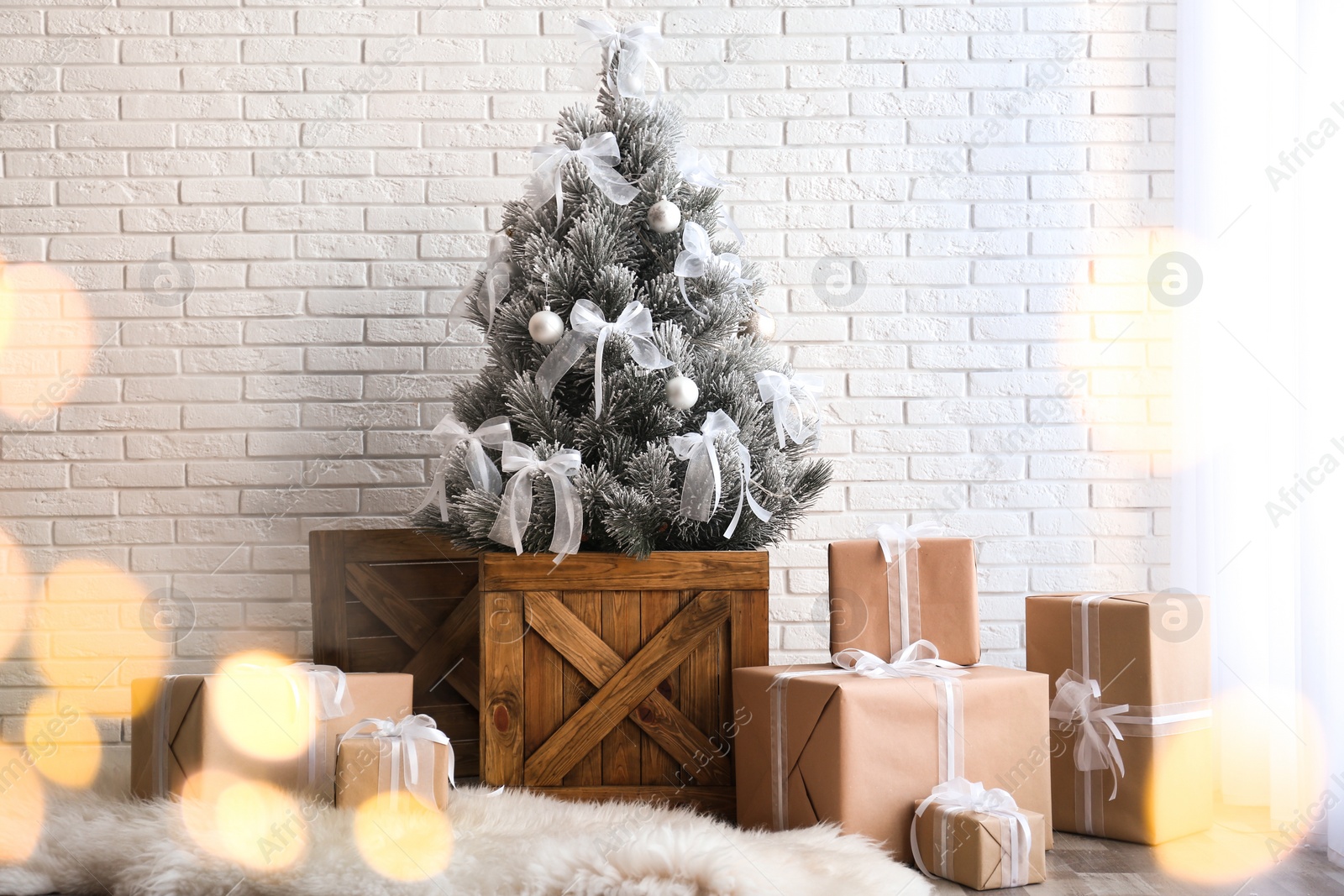 Photo of Stylish room interior with beautiful Christmas tree and gifts near white brick wall. Bokeh effect