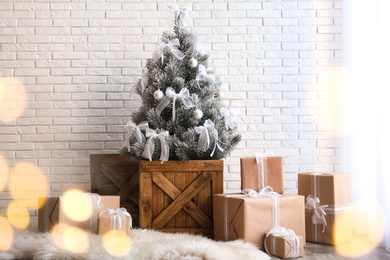 Photo of Stylish room interior with beautiful Christmas tree and gifts near white brick wall. Bokeh effect