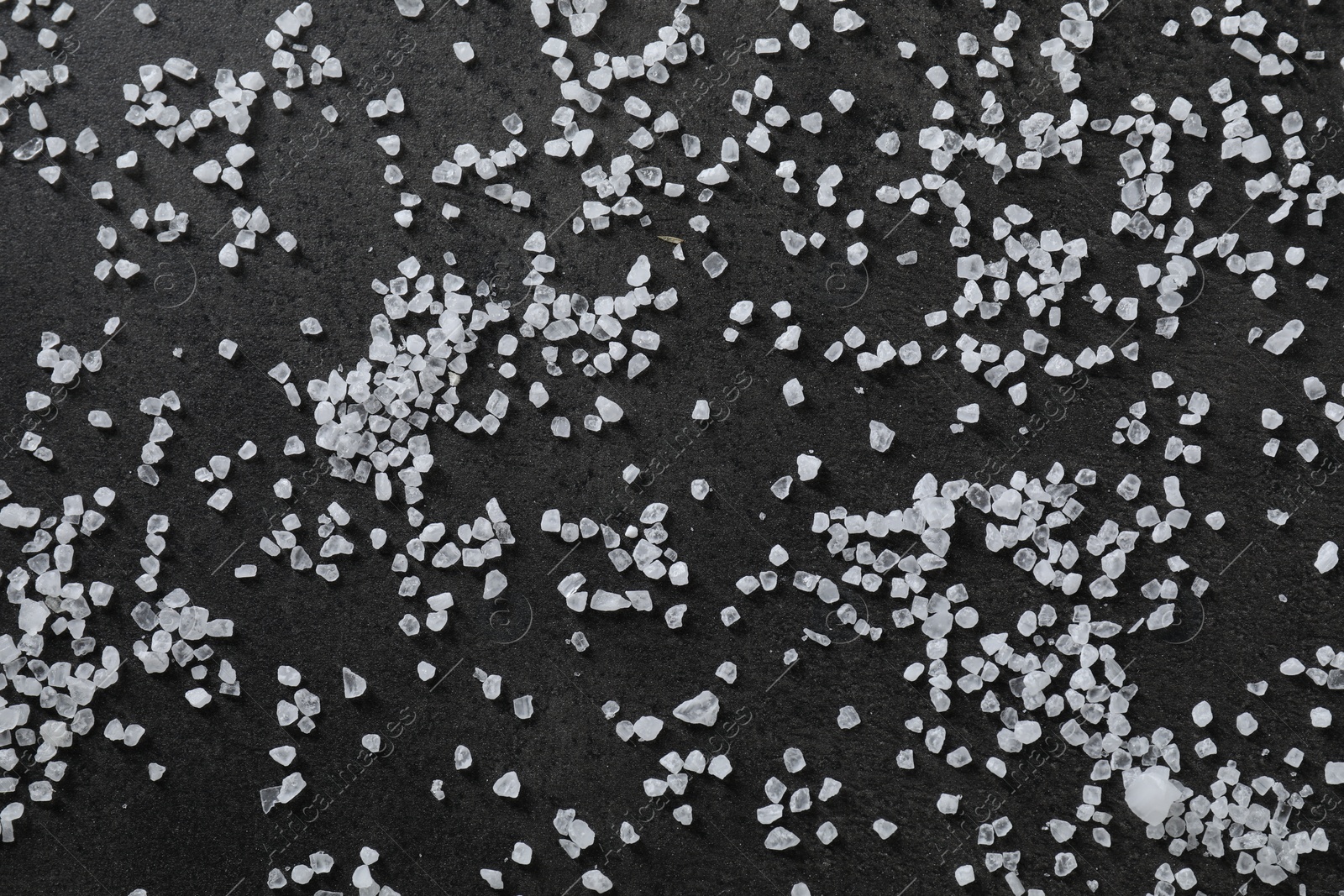 Photo of Scattered white natural salt on black table, top view