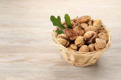 Wicker basket with tasty dried figs and green leaf on light wooden table. Space for text