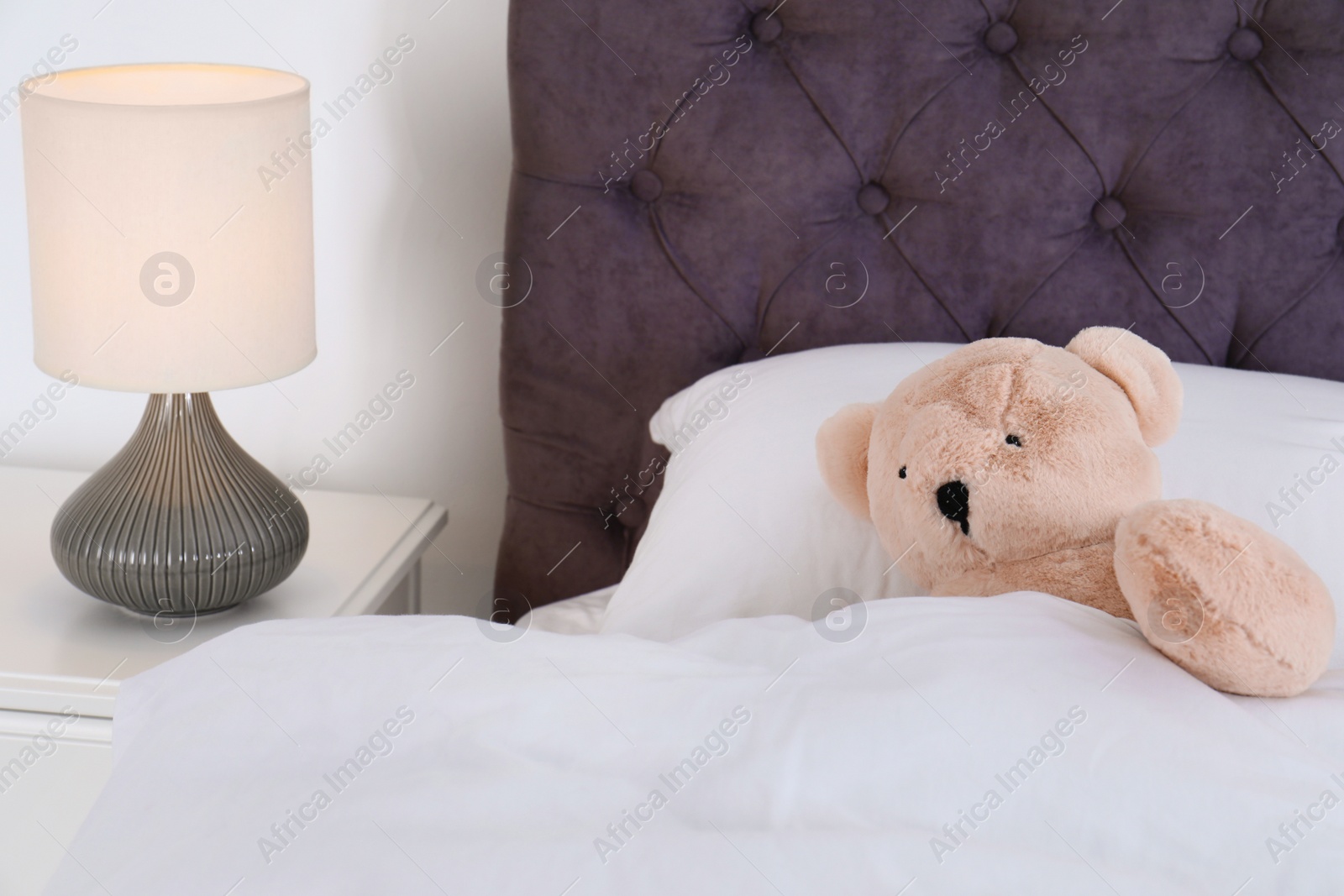 Photo of Cute teddy bear lying in bed indoors. Space for text