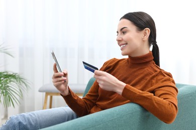 Photo of Happy young woman with smartphone and credit card shopping online on sofa at home