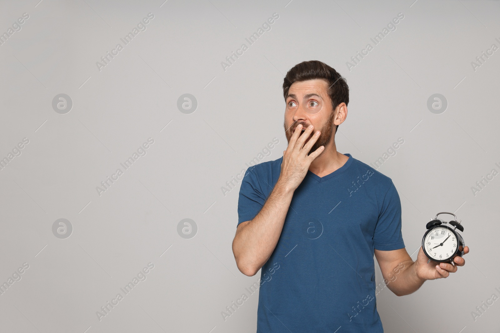 Photo of Emotional bearded man with alarm clock on light grey background, space for text. Being late concept