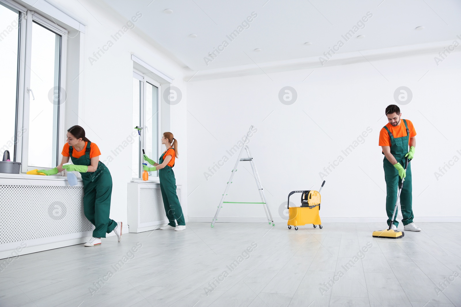 Photo of Team of professional janitors in uniforms cleaning room