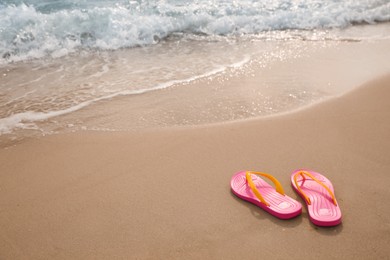 Bright pink beach slippers on sand near sea, space for text