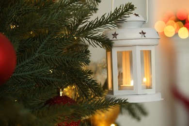 Christmas lantern with burning candle on fir tree indoors, closeup