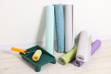 Photo of Different wallpaper rolls, roller and tray near white wall indoors