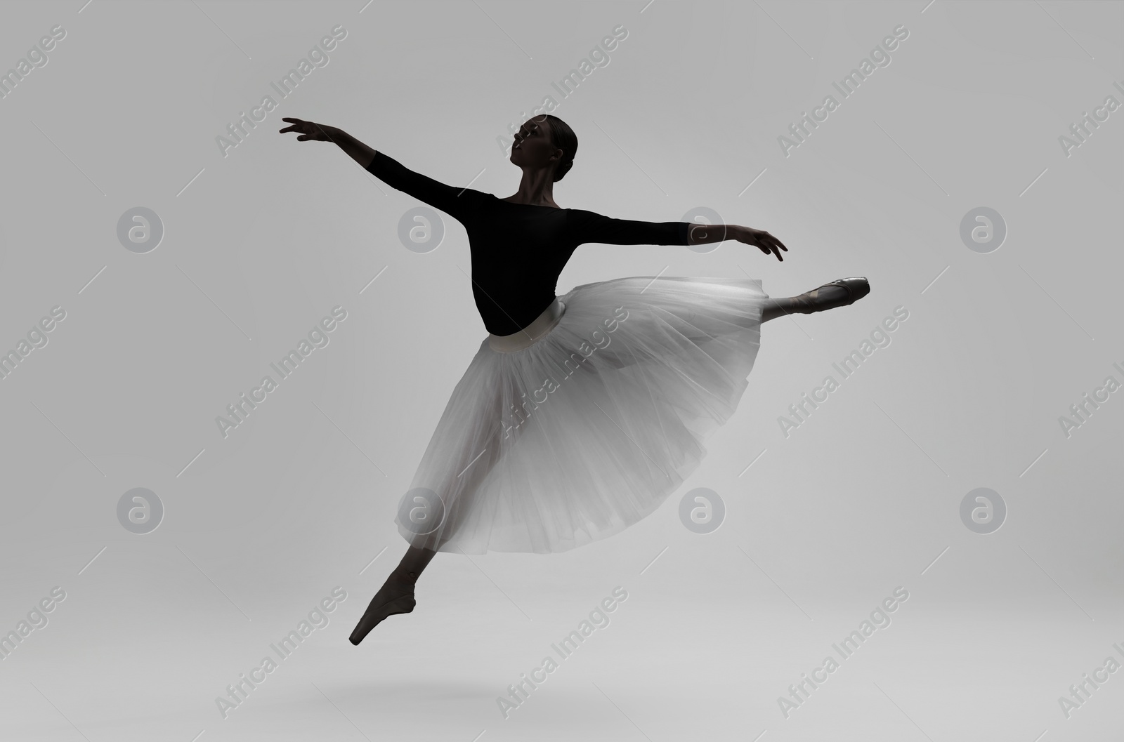 Image of Beautiful ballerina dancing on light grey background. Dark silhouette of dancer