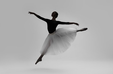 Image of Beautiful ballerina dancing on light grey background. Dark silhouette of dancer