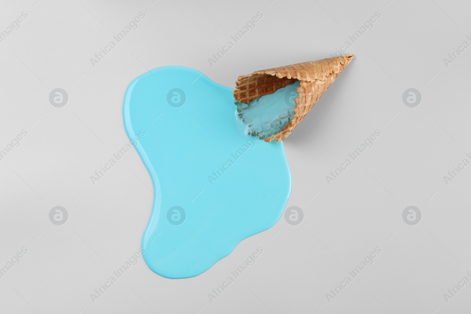 Photo of Melted ice cream and wafer cone on light blue background, top view