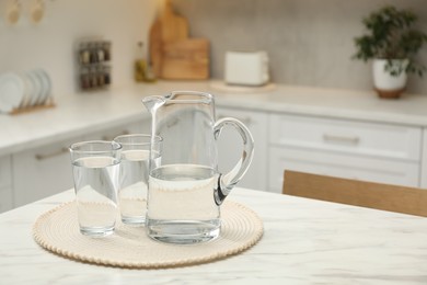 Jug and glasses with clear water on white table in kitchen, space for text