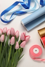 Photo of Making beautiful bouquet. Fresh tulips, ribbons and wrapping paper on white wooden table, flat lay