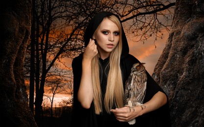 Witch wearing black mantle with owl in forest. Fantasy world