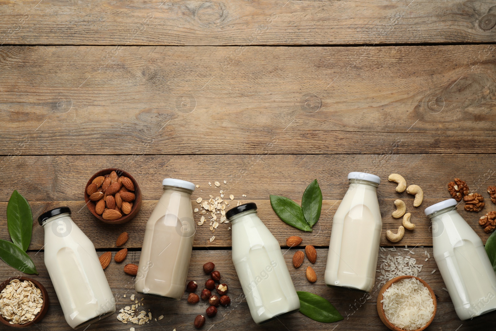 Photo of Different vegan milks and ingredients on wooden table, flat lay. Space for text