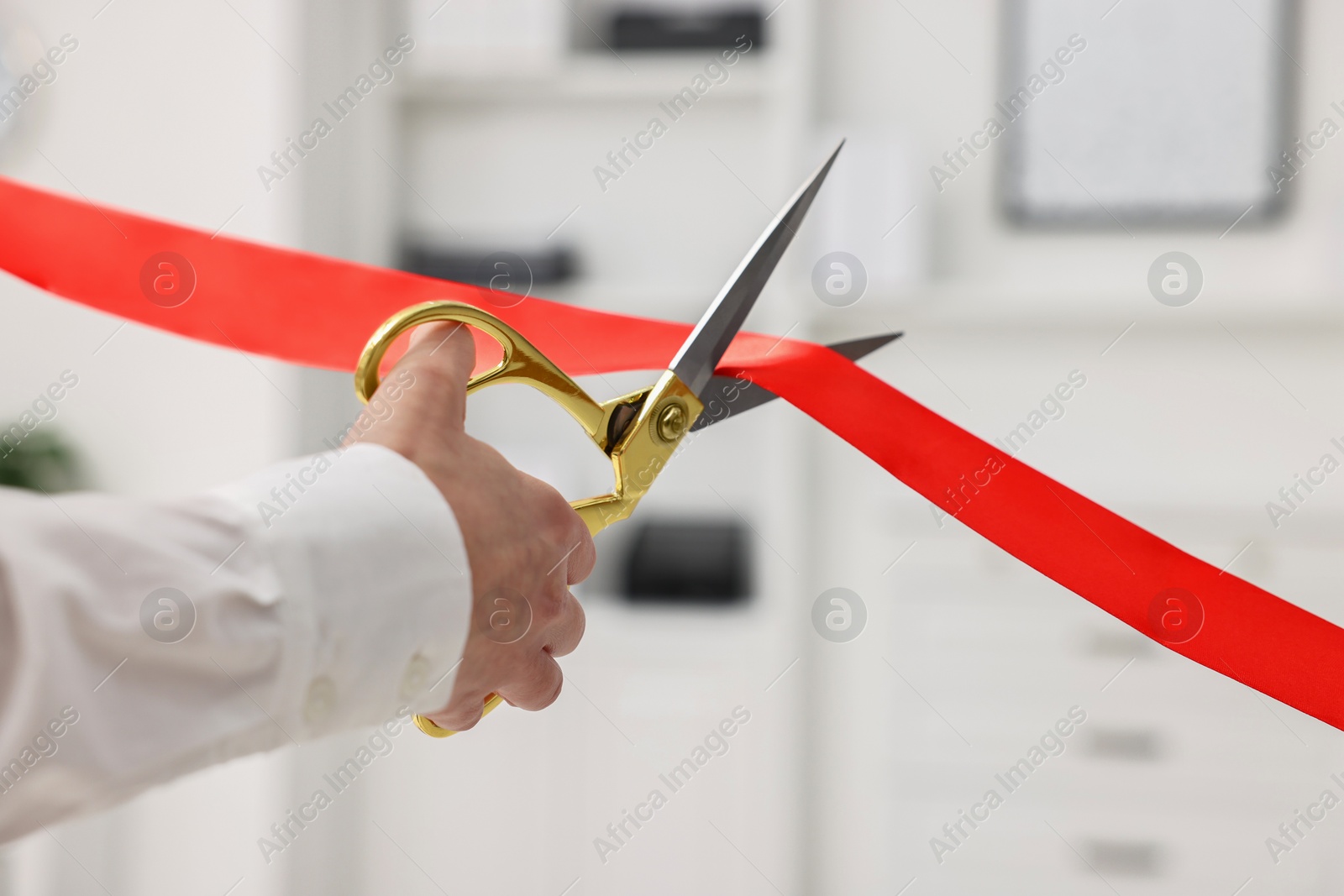 Photo of Woman cutting red ribbon with scissors indoors, closeup