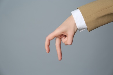 Photo of Businesswoman imitating walk with hand on grey background, closeup. Finger gesture