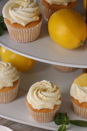 Photo of Delicious lemon cupcakes with white cream and lemons on table, closeup