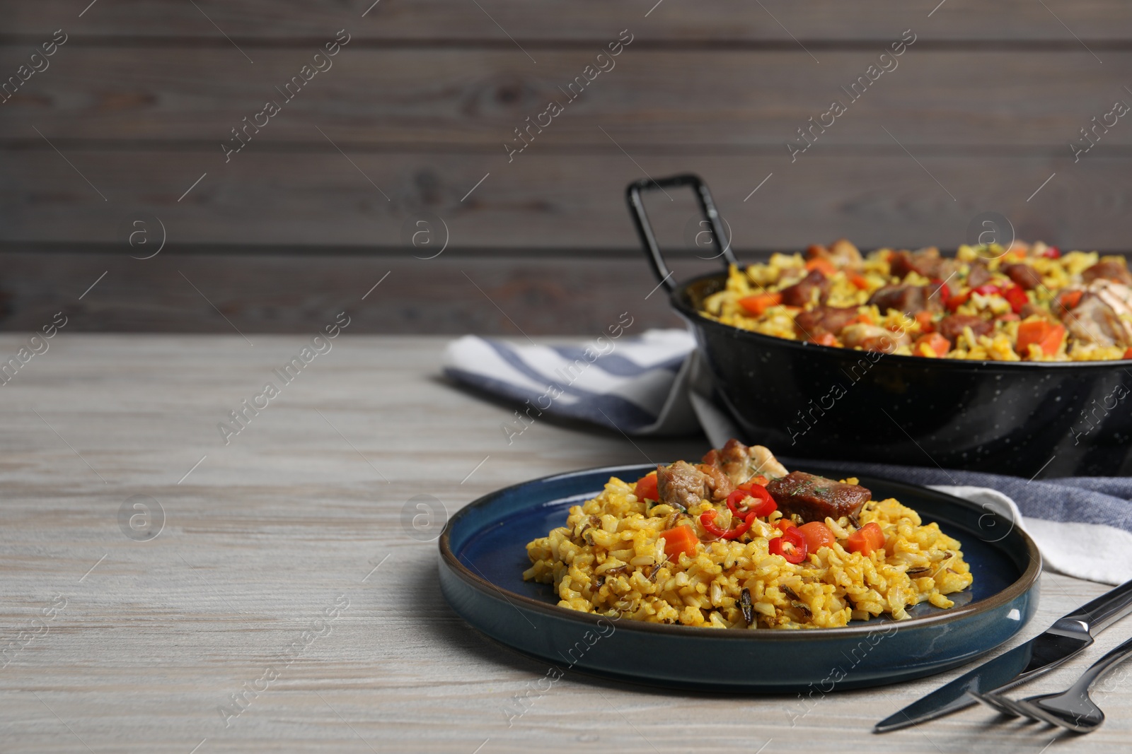 Photo of Delicious pilaf with meat, carrot and chili pepper on wooden table. Space for text