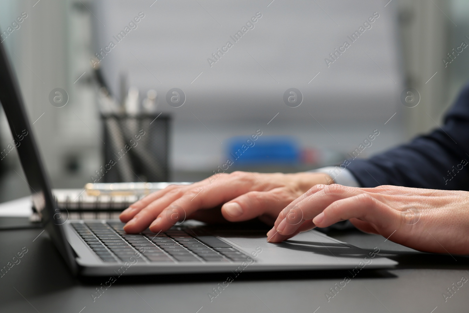 Photo of Woman working on laptop at black desk in office, closeup