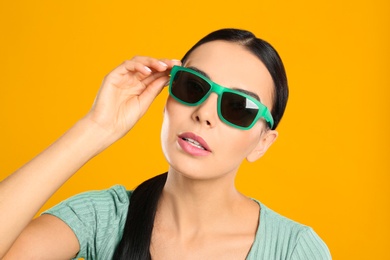 Photo of Beautiful woman wearing sunglasses on yellow background, closeup