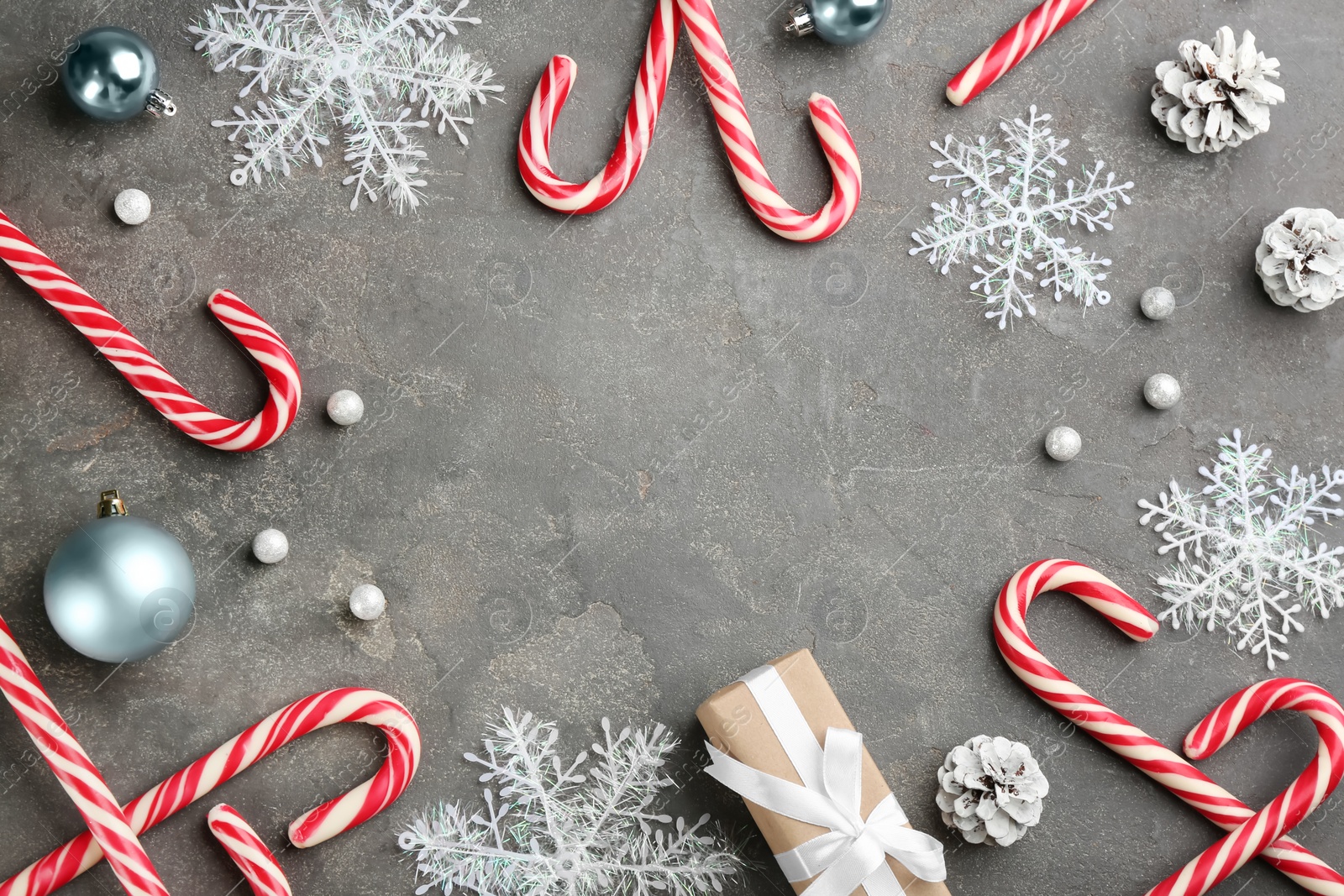 Photo of Frame of candy canes, gift box and Christmas decor on grey table. Space for text