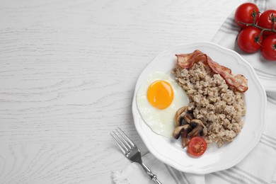 Photo of Tasty boiled oatmeal with fried egg, mushrooms, bacon and tomato served on white wooden table, flat lay. Space for text