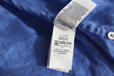 Photo of Clothing label in different languages on blue garment, closeup