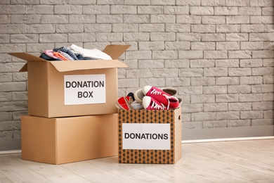 Photo of Donation boxes with clothes and shoes on floor against brick wall