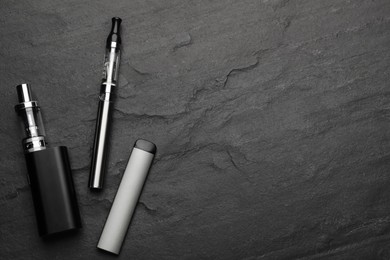 Photo of Electronic smoking devices on black background, flat lay. Space for text