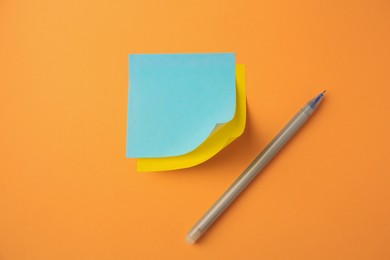 Photo of Blank paper notes and pen on pale orange background, flat lay