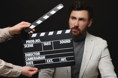 Photo of Actor performing while second assistant camera holding clapperboard on black background, closeup
