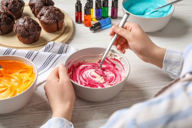 Photo of Woman mixing cream with pink food coloring at white wooden table, closeup. Decorate cupcakes