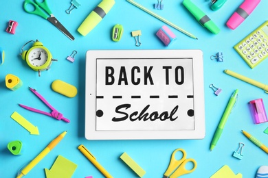 Tablet with phrase "BACK TO SCHOOL" and different stationery on blue background, flat lay