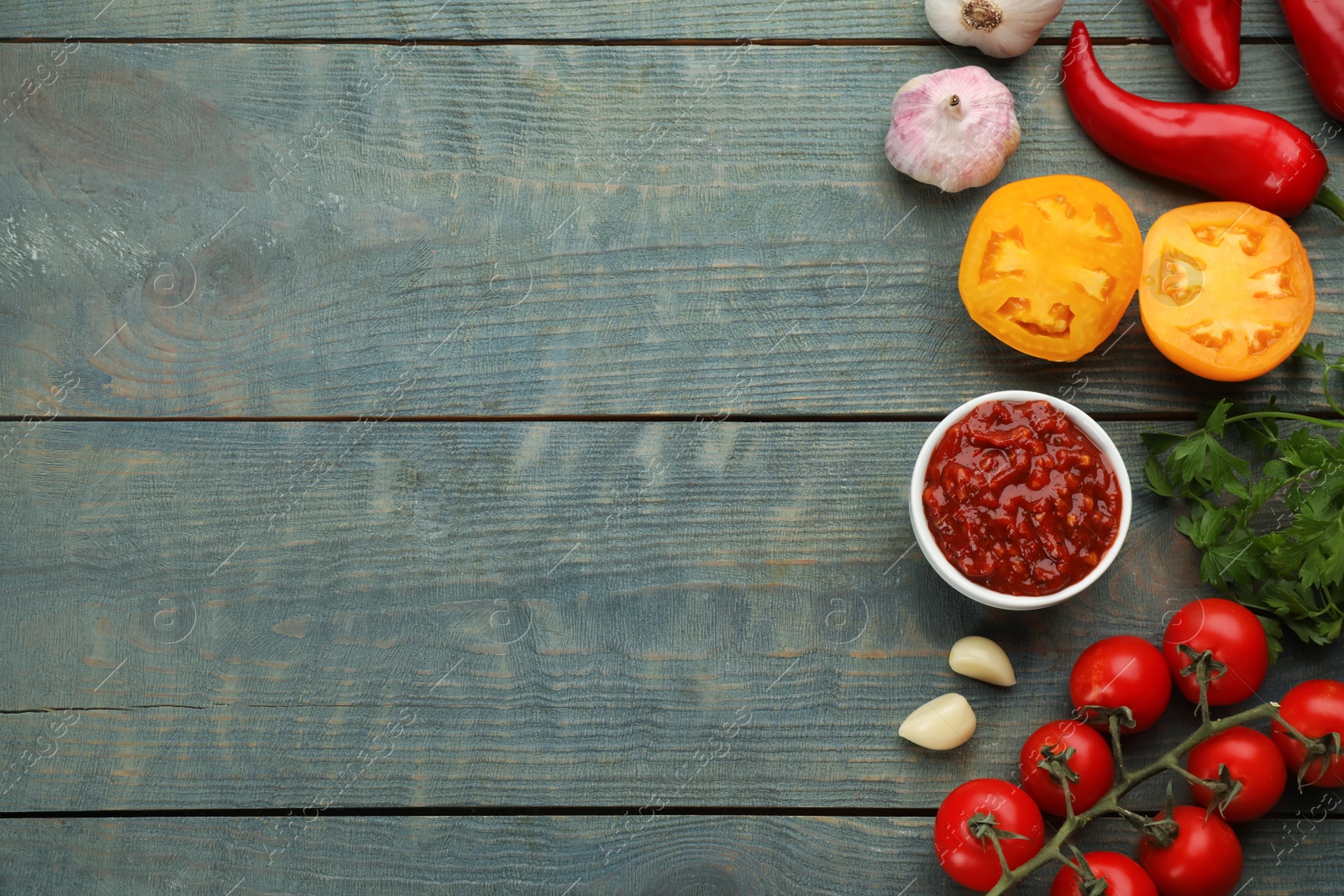 Photo of Delicious adjika sauce in bowl and ingredients on light blue wooden table, flat lay. Space for text