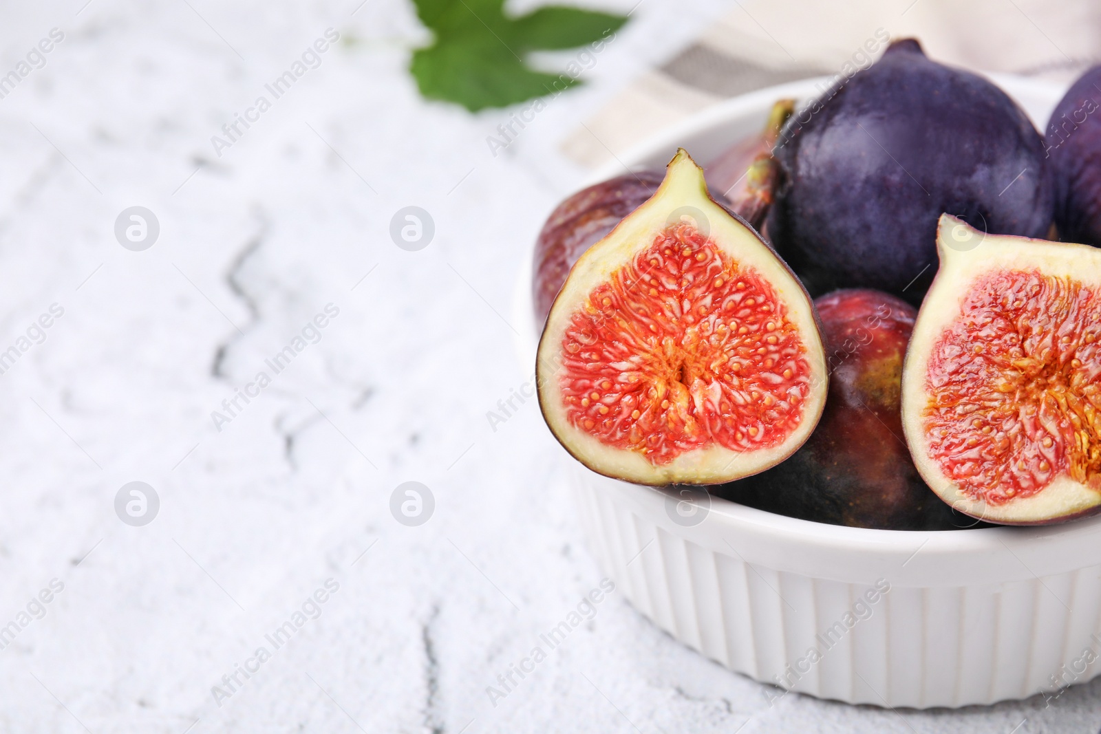Photo of Bowl of tasty ripe figs on white textured table, closeup. Space for text