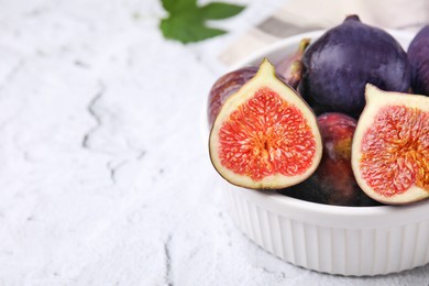 Bowl of tasty ripe figs on white textured table, closeup. Space for text